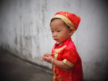 Cute baby boy wearing traditional clothing while looking away against wall