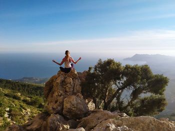 Man sitting on rock by mountain against sky