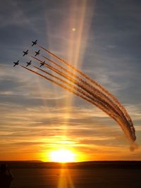 Low angle view of airshow against sky during sunset