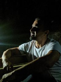 Man looking away while sitting on sofa at night