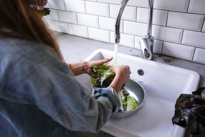 Cropped image of woman washing lettuce at sink in kitchen