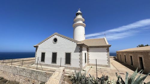 Lighthouse by sea against clear blue sky