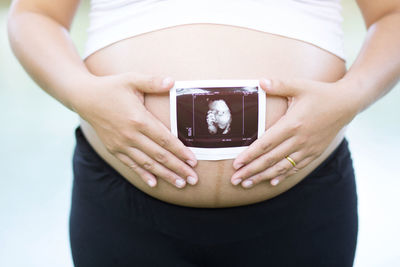 Midsection of pregnant woman holding ultrasound on stomach