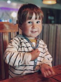 Portrait of a curious boy wearing a striped t-shirt looking at the camera sitting at cafe table 