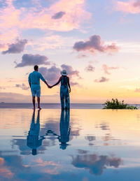 Rear view of man standing at beach against sky during sunset