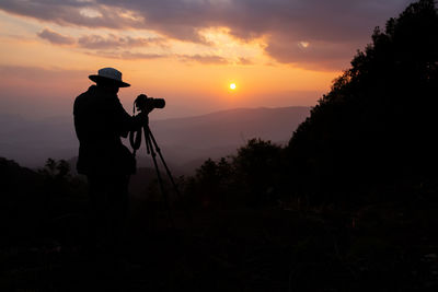 Silhouette man photographing against sky during sunset