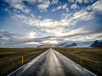 Country road amidst landscape against sky