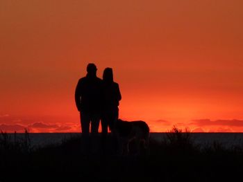 Silhouette man standing on field against orange sky