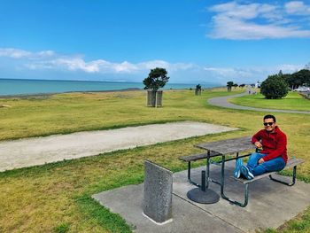 Smiling man sitting on bench against sky