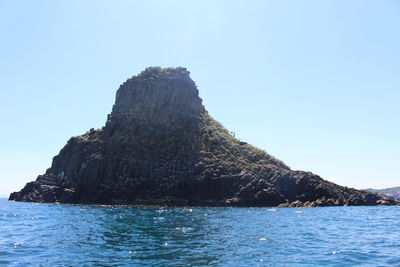 Rock formation in sea against clear sky