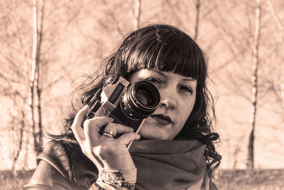 Portrait of woman holding camera against bare trees