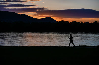 Silhouette man running at lakeshore against mountains