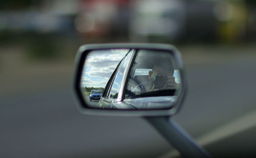 Reflection of man photographing on side view mirror of car