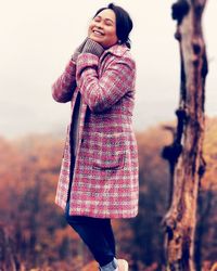 Smiling mid adult woman with eyes closed standing against trees