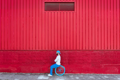 Side view of calm hipster bearded male sitting in bicycle wheel on the street near red background