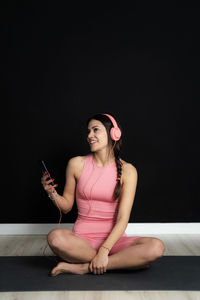 Young woman using mobile phone while sitting against black background