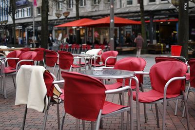 Empty chairs and tables at sidewalk cafe against buildings in city