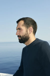 Young man looking away against sea against clear sky