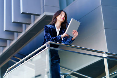 Portrait of young woman using mobile phone while standing on staircase