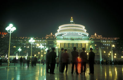 Rear view of businessmen standing next to illuminated building