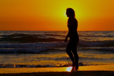 Silhouette woman standing on beach against orange sky