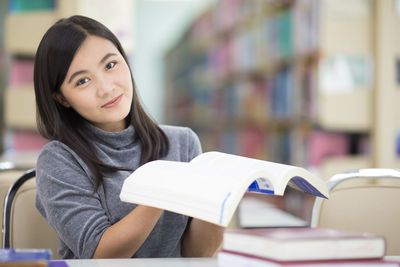 Young woman reading book while sitting at table in library