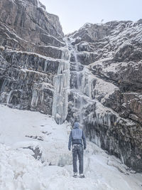 Rear view of man walking on snow covered mountain and frozen waterfall