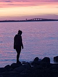 Rear view of silhouette man standing on rock against sea