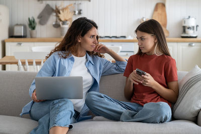 Smiling friends using phone while sitting at home