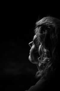 Close-up of woman looking away against black background