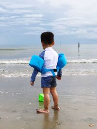 Rear view of toddler with water wings standing on shore at beach
