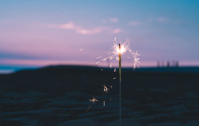 Firework display on land against sky at sunset