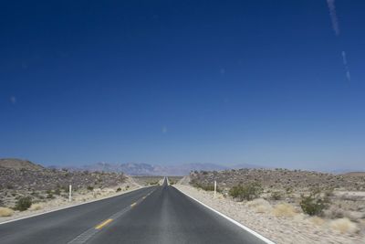 Road passing through landscape against clear blue sky