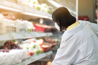 Woman wearing mask by fruits in store