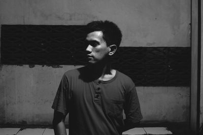 Young man looking away while standing against wall