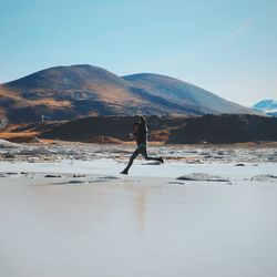 Side view of man jumping over salt lake on sunny day