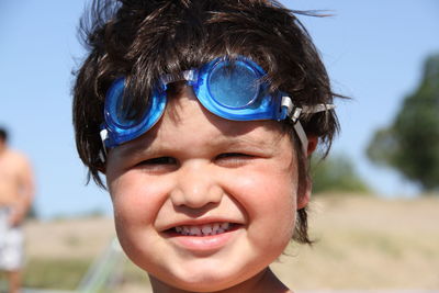 Close-up portrait of smiling boy wearing swimming goggles against sky