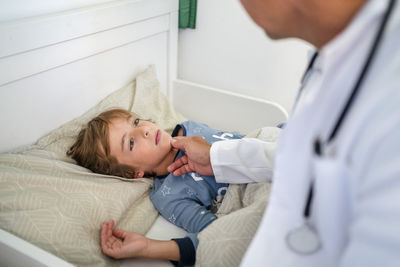 Doctor examining boy in bed at home