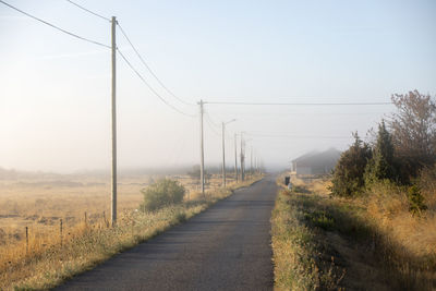 View of power line along country road at foggy day