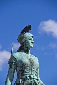 Low angle view of bird perching on statue against blue sky