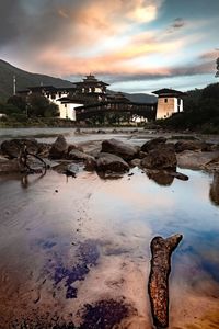 Old building by beach against sky during sunset