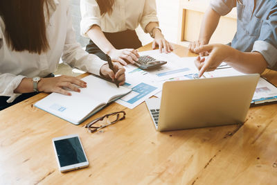 Midsection of businessman pointing at laptop while client sitting on table at office