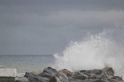 Waves splashing on rocks against sky
