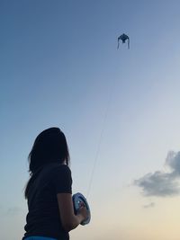 Rear view of woman flying kite at sunset