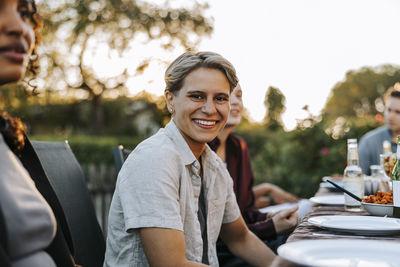 Portrait of smiling young woman with short hair sitting near table in back yard at social party