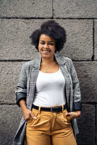 Portrait of a smiling young woman standing against wall