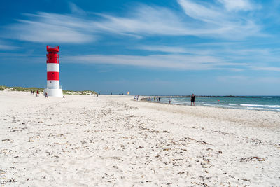 Lighthouse on beach by sea against sky