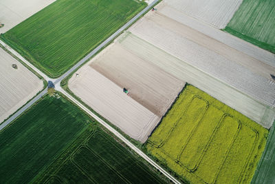 Drone aerial view of some fields of rapeseed and cereal crops and two tractors plowing the soil.
