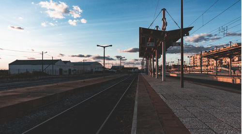 Railroad station platform against sky at sunset