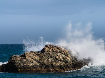 Sea waves splashing on rock against sky